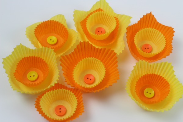 A  number of yellow and orange cake cases layered to look like daffodil flowers with buttons in the center 