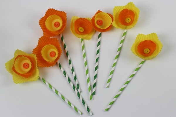 A  number of yellow and orange cake cases layered to look like daffodil flowers with buttons in the center  and paper straws as stems 