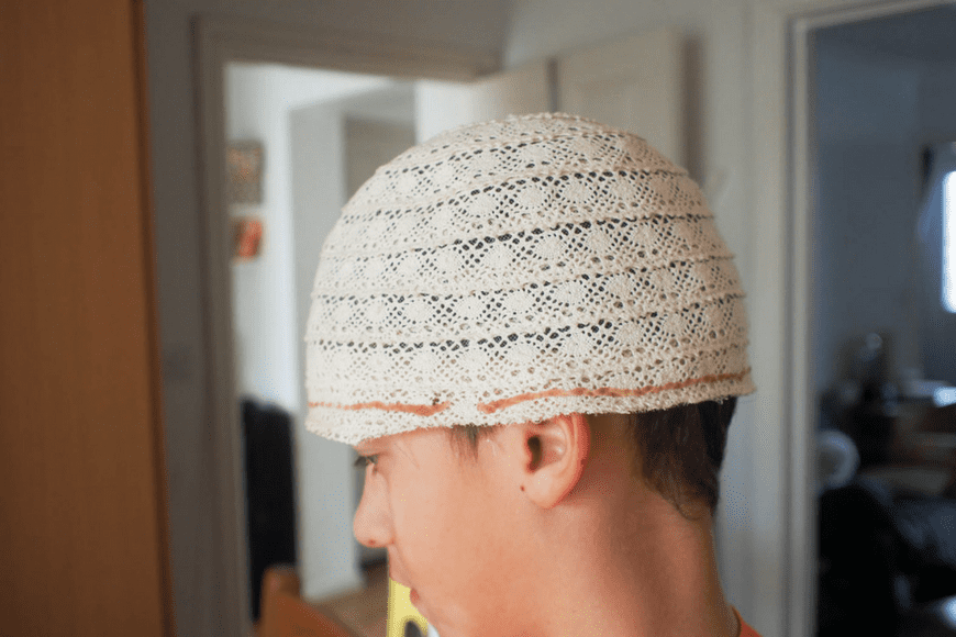 Cut the brim off a light-colored baseball hat. 2. Put a hat on and drape a sheet over your head. 3. Mark where your eyes are, then pull the sheet off. 4. Remove the sheet and hat and pin them together.
