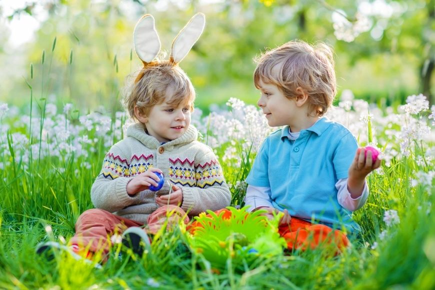 Two small boys, one with bunny ears sat in the grass with their easter eggs